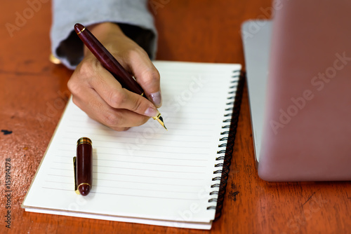 Beautiful businesswoman writing on papers in a notebook with a pen signing. Business and Technology Concepts.