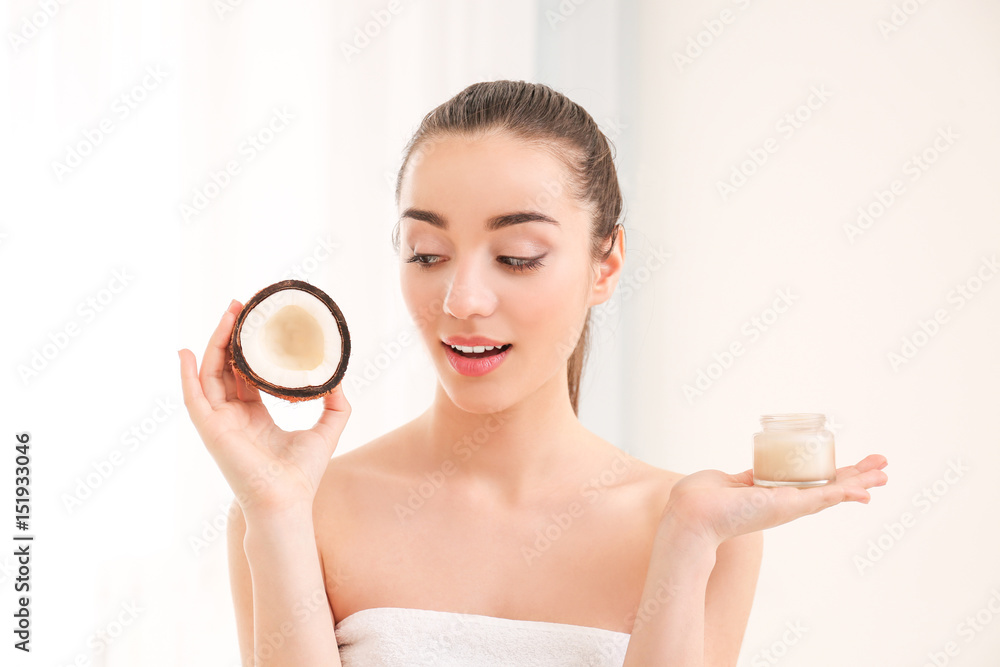 Beautiful young woman holding coconut oil and fresh nut on light background Beautiful young woman holding coconut oil and fresh nut on light background