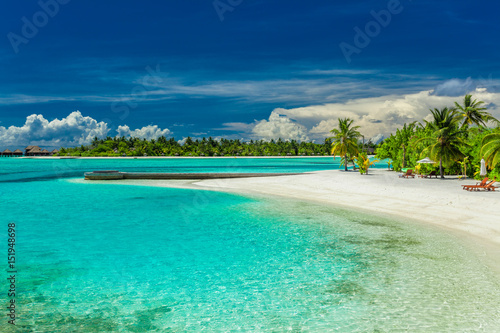 Palm trees and beach umbrelllas over lagoon and sandy beach, Maldives island