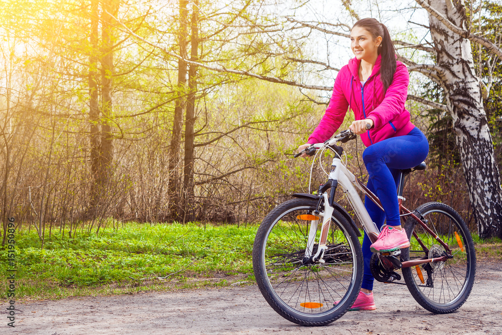Young woman rides a bike along a path in the forest at sunset of a summer day