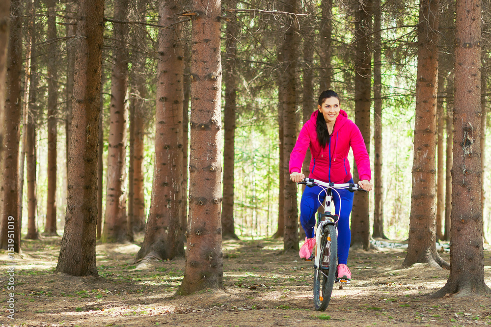 A woman is riding a bicycle in a pine forest A woman is riding a bicycle in a pine forest