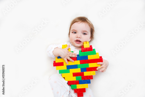 baby cute girl holds heart with lots of colorful plastic blocks constructor. Love heart for valentine background. .