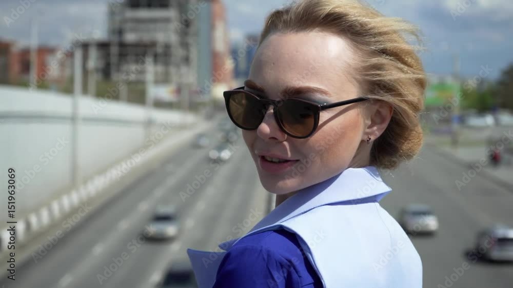Beautiful business woman in a business suit with glasses and a short haircut, stands on the bridge. Movement of cars. Beautiful business woman in a business suit with glasses and a short haircut, stands on the bridge. Movement of cars.