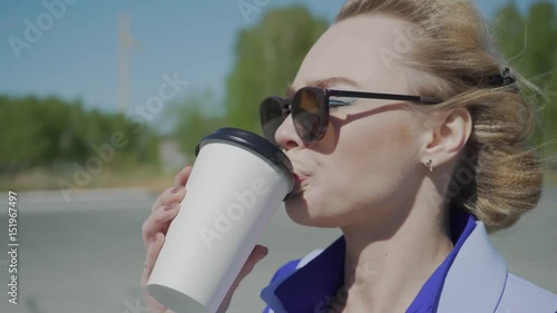 Cheerful stylish businesswoman drinking coffee outside on urban background photo