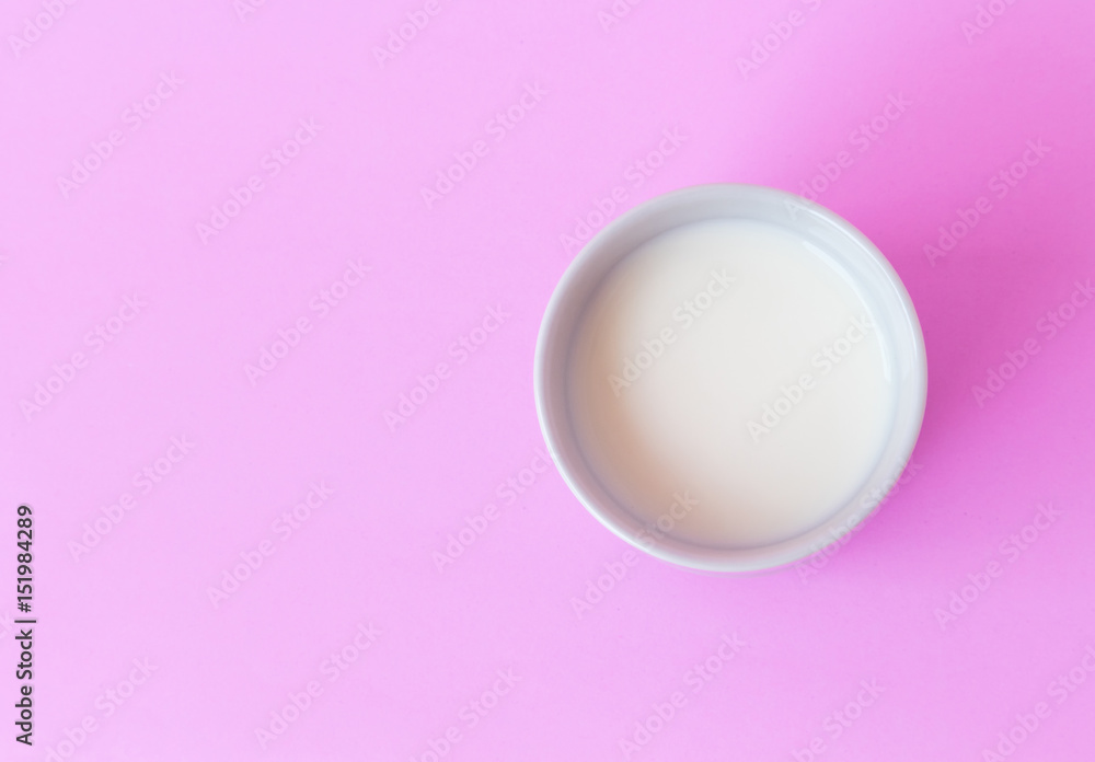 Closeup top view milk in white ceramic cup on pink background, selective focus Closeup top view milk in white ceramic cup on pink background, selective focus
