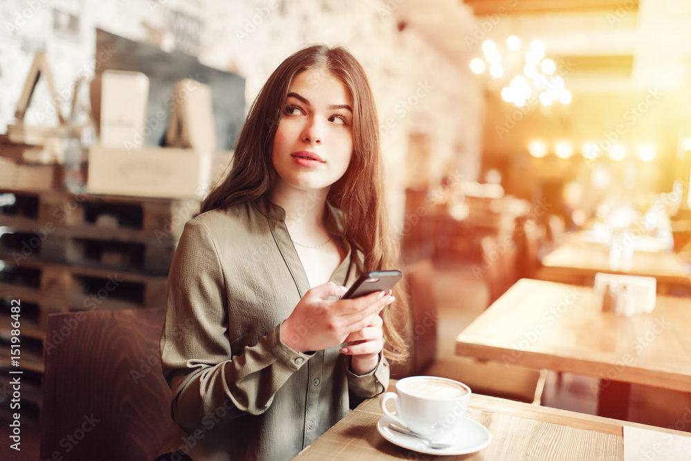 Pretty girl using cell phone smiles and looks over her shoulder out of frame.In caffe.With coffe.