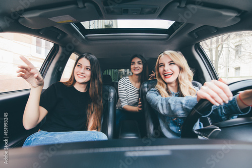 Three beautiful young cheerful women looking at pointed hand direction with smile while sitting in car © F8  \ Suport Ukraine