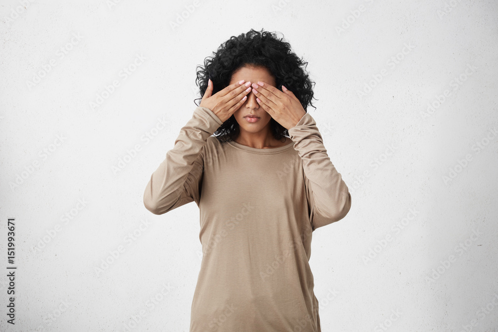 © wayhome.studio  - Human feelings, reaction and attitude. Body language. Studio shot of dark-skinned young female with black curly hair covering eyes with both hands, doesn't want to see anything or feeling ashamed