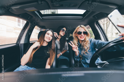 View of Three beautiful young cheerful women making selfie and smiling while sitting in car together © F8  \ Suport Ukraine