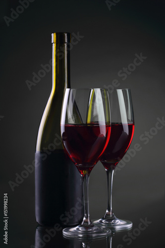Wine glass and bottle with red wine on gray