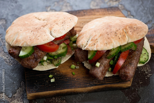 Rustic wooden serving board with grilled cevapcici sausages and vegetables in pita bread, studio shot