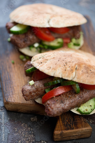 Close-up of pitas with bbq cevapi or cevapcici sausages and vegetables, vertical shot