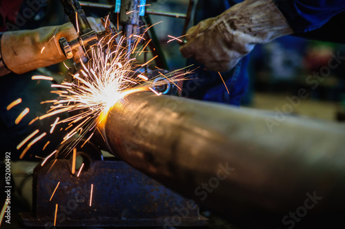 Worker cutting steel pipe with acetylene welding cutting torch and bright sparks in steel construction industry. photo