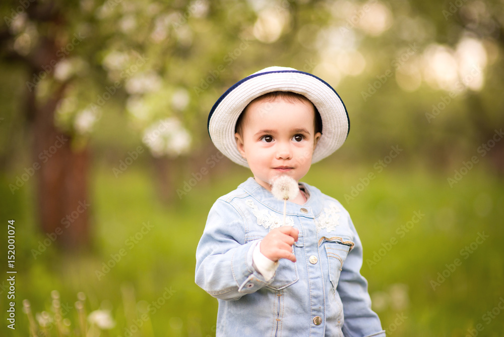 Little girl in a hat with a dandelion on a walk in a spring park or garden Little girl in a hat with a dandelion on a walk in a spring park or garden