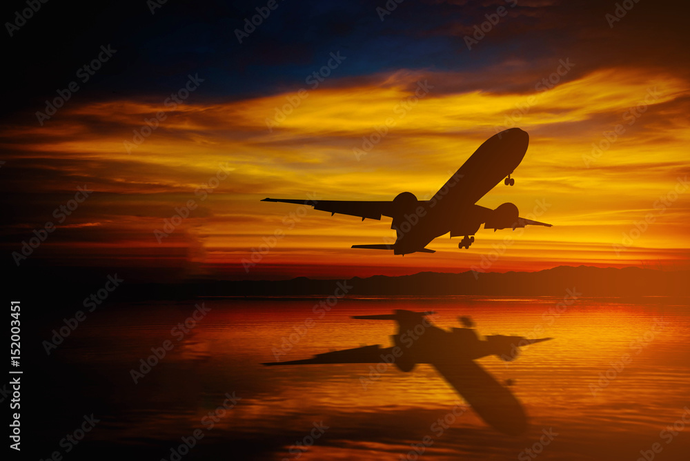 Silhouette of plane fly over sea on dramatic sky during sunset.