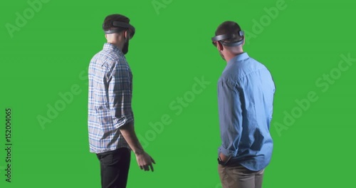 Back view of young adult Caucasian colleagues using holographic augmented reality glasses together. Green screen chroma key. 4K UHD RAW edited footage photo