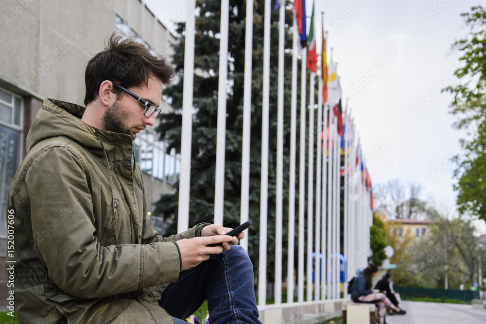 young man working texting in a mobile phone sitting on a bench in the square young man working texting in a mobile phone sitting on a bench in the square