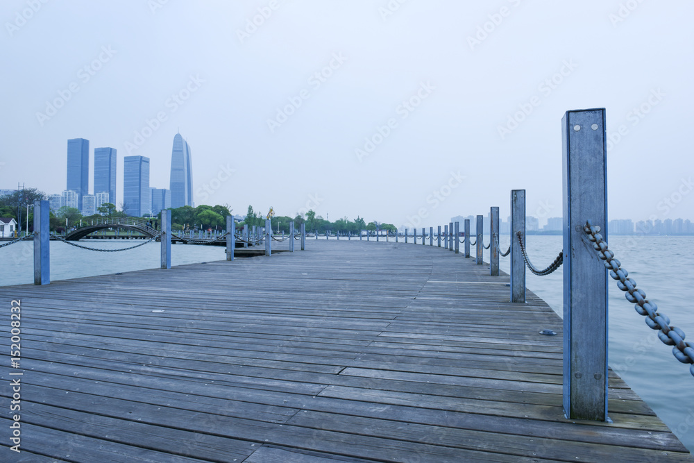 Wooden plank bridge across the water and modern city background.