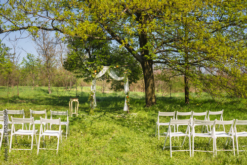 Wedding arch consist of withe, wooden constructions. Decorated by flowers and oranges. Rustic style