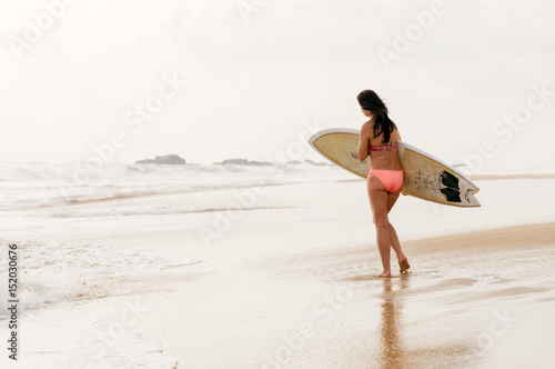 Young lady walking with surf board on sandy tropical beach. Sri Lanka. Hikkaduwa