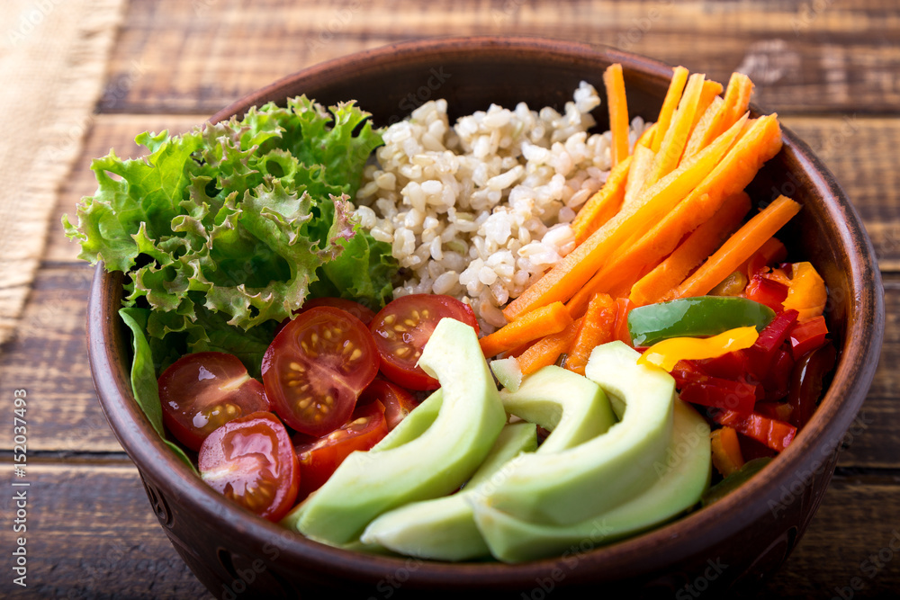 Vegan buddha bowl on wooden background. Bowl with carrot, lettuce, tomatoes cherry, pepper, avocado and porridge. Vegetarian, healthy, detox food concept. Vegan buddha bowl on wooden background. Bowl with carrot, lettuce, tomatoes cherry, pepper, avocado and porridge. Vegetarian, healthy, detox food concept.