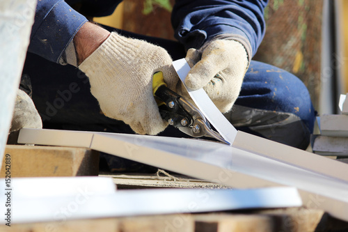 The worker makes the sladding of windows in the restored building in the city, cuts the metal sheet for the slope with scissors. photo