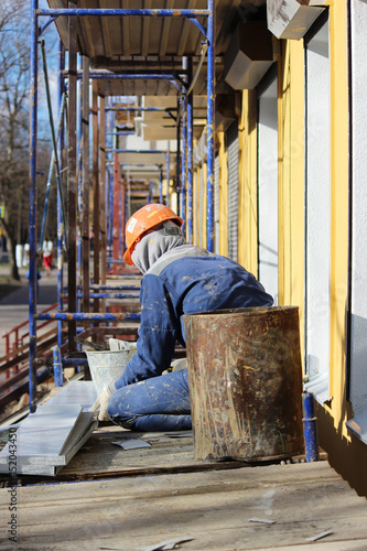 The worker makes the sladding of windows in the restored building in the city, cuts the metal sheet for the slope with scissors. photo