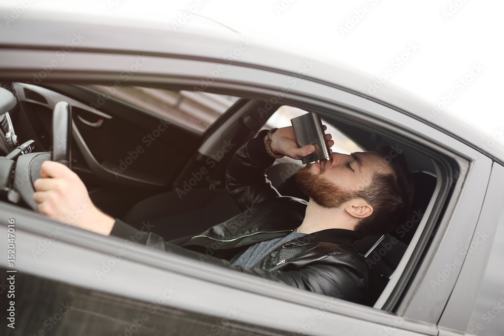 Drunk driver driving a car. Driving in a state of intoxication.Young man driving a car with an iron flask with alcohol. Drunk driver driving a car. Driving in a state of intoxication.Young man driving a car with an iron flask with alcohol.
