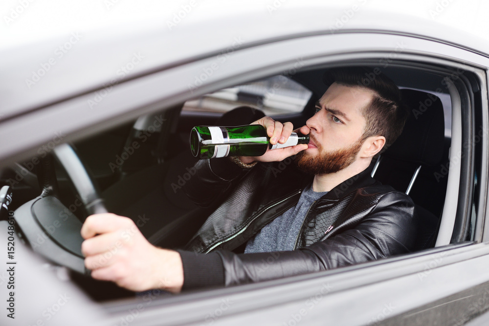 Drunk young man with a beard with a bottle of beer in his hand behind ...