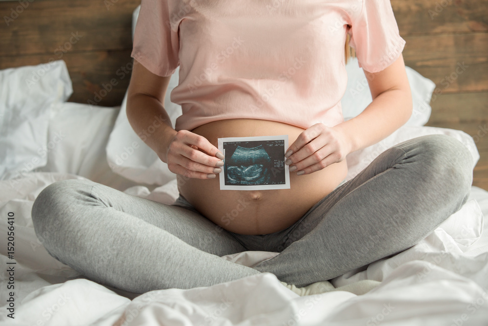 Young preganant woman expecting a baby relaxing on bed indoors Young preganant woman expecting a baby relaxing on bed indoors