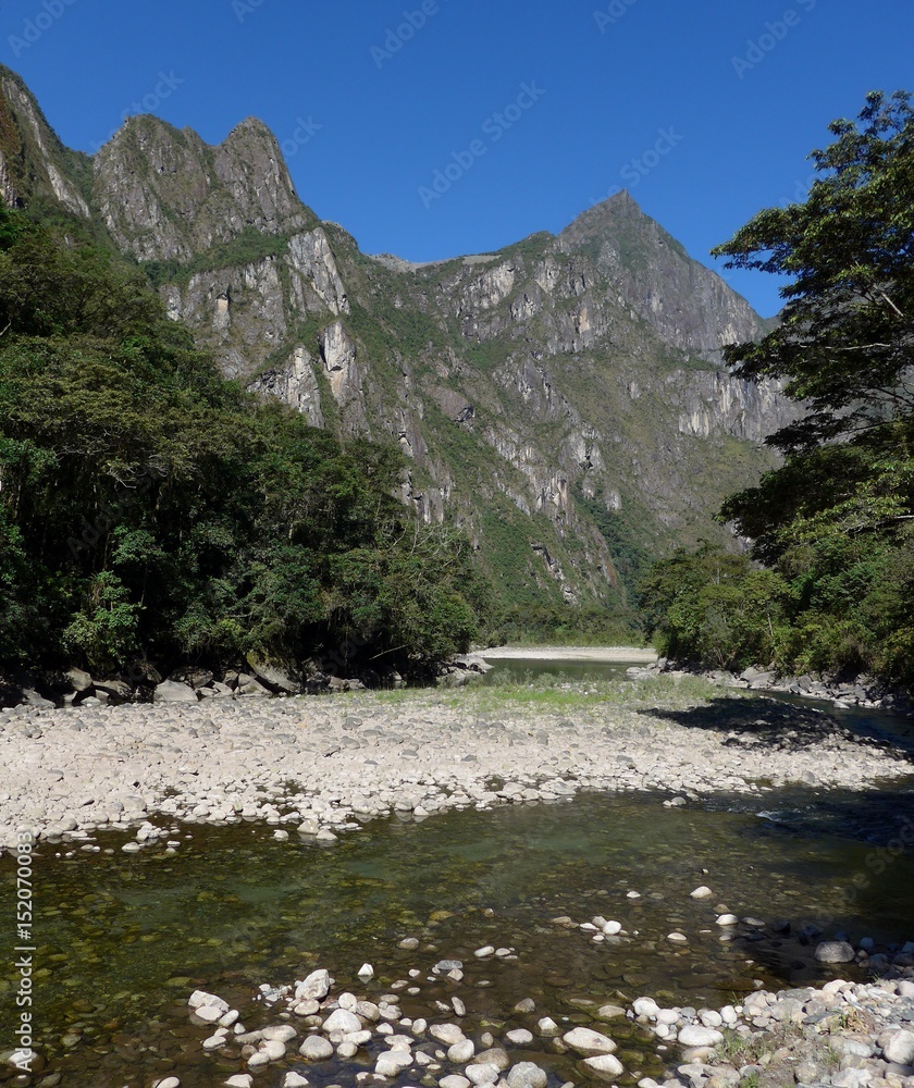 Mountains towering over a tranquil river on a beautiful blue sky day. 