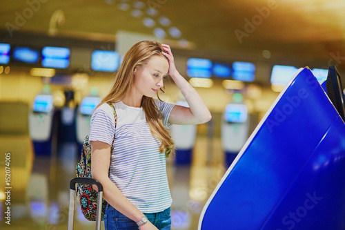 Unhappy tourist girl in international airport, doing self check-in