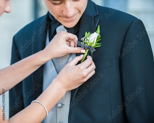 Handsome Mexican teen receiving help with boutonniere on formal black suit.