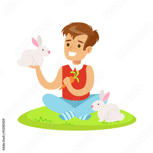Smiling boy sitting on green grass, playing and feeding two white rabbits with carrot. Colorful cartoon character vector Illustration