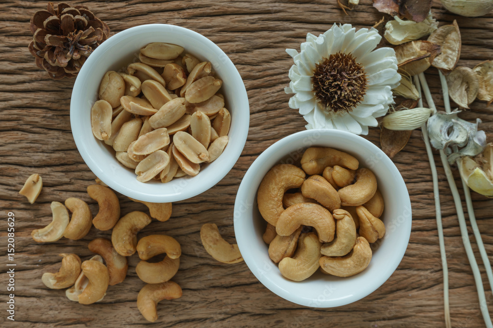 Roasted cashew nuts and peanuts appetizer in white bowl on wooden table background Roasted cashew nuts and peanuts appetizer in white bowl on wooden table background