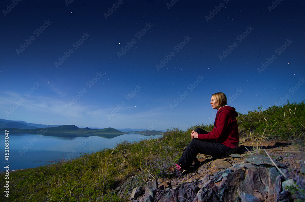 Fototapeta premium A lake with a gentle rocky shore at night. The girl is sitting on the lake.