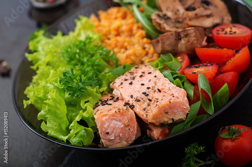 Healthy salad with salmon, tomatoes, mushrooms, lettuce and lentil on dark background