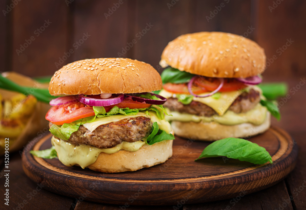 Big sandwich - hamburger with juicy beef burger, cheese, tomato,  and red onion on wooden background