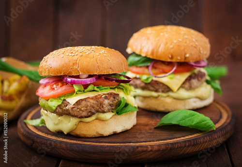 Big sandwich - hamburger with juicy beef burger, cheese, tomato, and red onion on wooden background