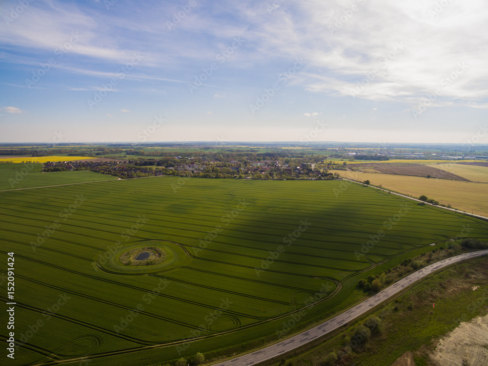 
Aerial view of green agricultural fields with a country road and a smal city under blue sky in germany