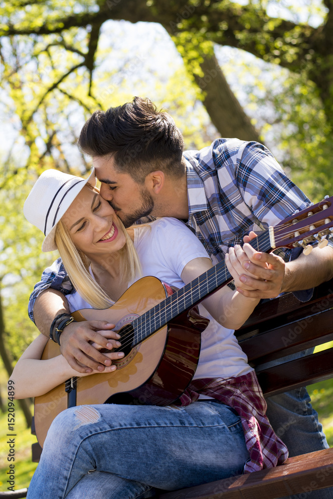 Couple sitting on the park bench playing guitar on beautiful sunny day