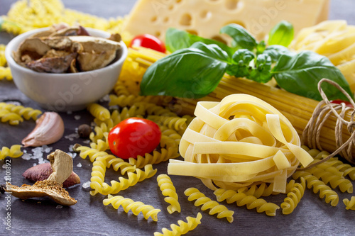 Various kinds of pasta ingredients with mushrooms, basil, cherry tomato, garlic, pepper, cheese on the kitchen wooden table. The concept of Italian food.