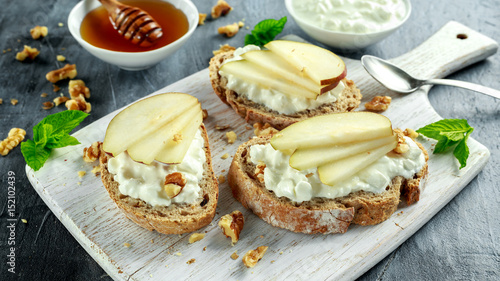 Appetizer bruschetta with pear, honey, walnut and cottage cheese on white board.