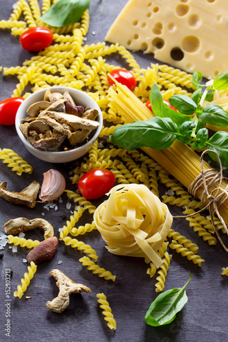 Different kinds of pasta with ingredients mushrooms, basil, cherry tomato, garlic, pepper, cheese on a kitchen wooden table. The concept of Italian food. photo