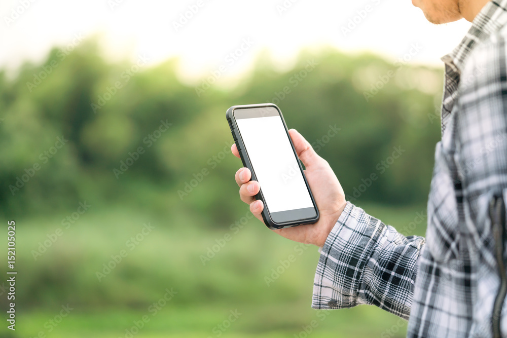 man holding smartphone in hands against green spring background 
A Man using his Mobile Phone outdoor, blank screen close up shot.