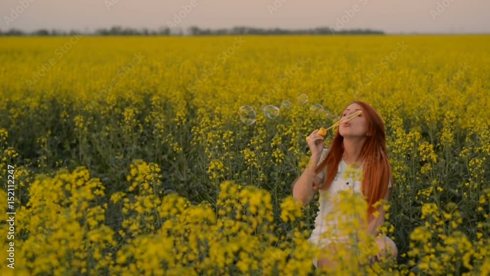 Young beautiful red-haired woman puffing bubbles in a flowering field, slow motion Young beautiful red-haired woman puffing bubbles in a flowering field, slow motion
