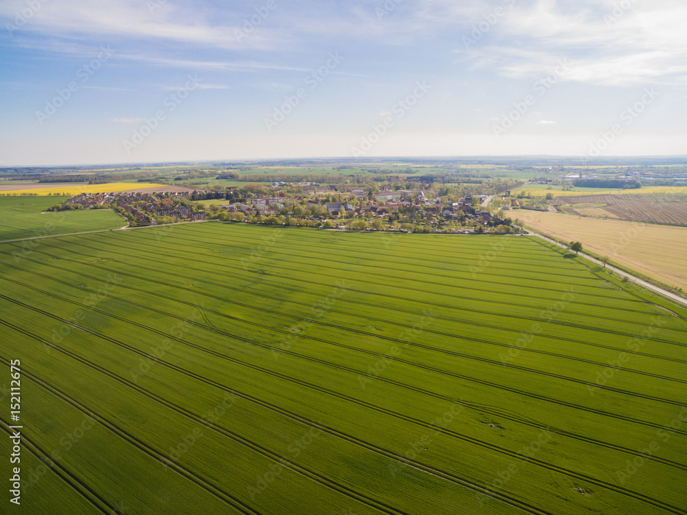  
Aerial view of green agricultural fields with a country road and a smal city under blue sky in germany
