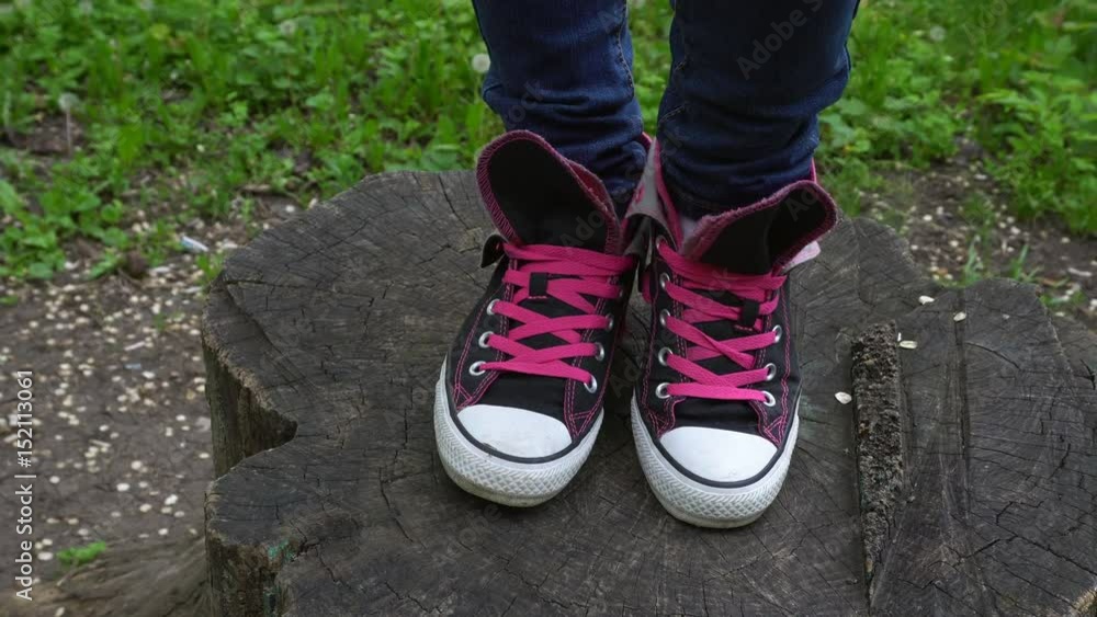 Female feet in sneakers moving and posing on stump in park. Steadycam shot. Female feet in sneakers moving and posing on stump in park. Steadycam shot.