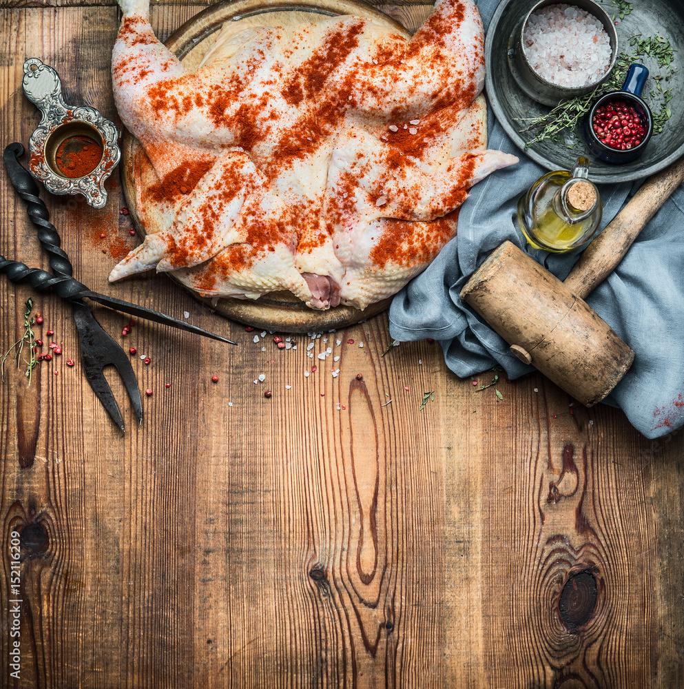 Whole chicken flattened out with condiment and kitchen tools on wooden rustic background
