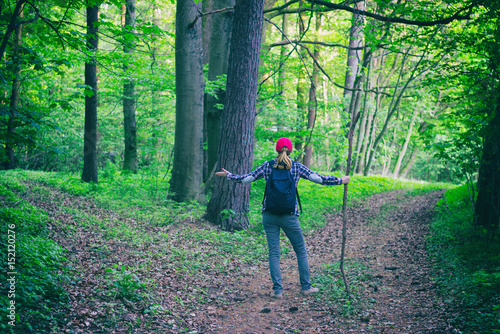 Young hiking woman does not know which way to go in green forest. A tourist girl lost herself on a hiking trip. Adventure concept.  photo